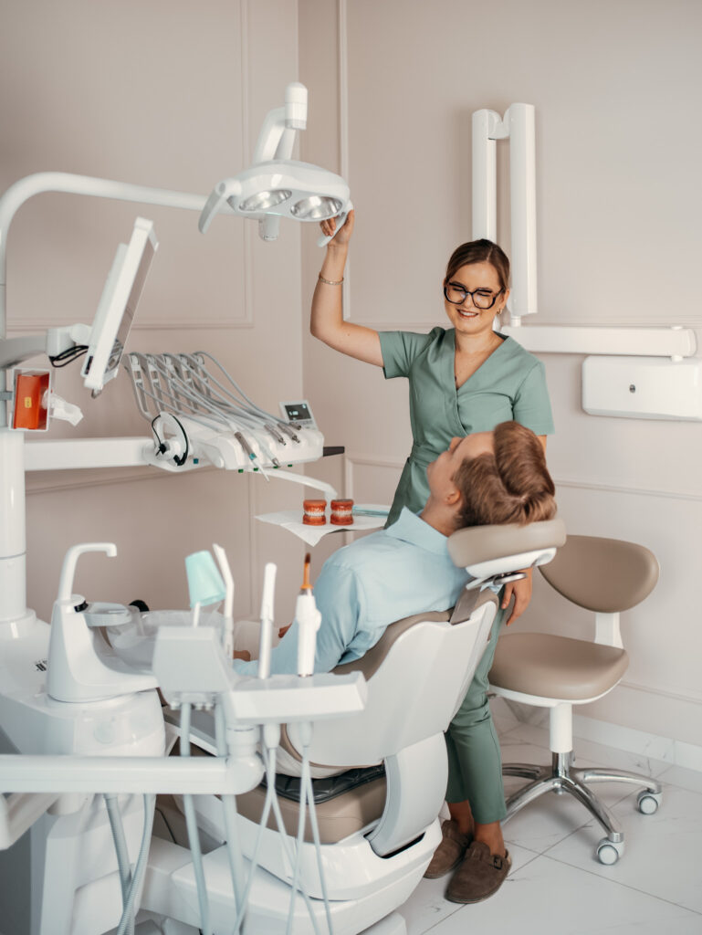 Stomatolog uśmiecha się i trzyma narzędzie nad leżącym pacjentem w nowoczesnym gabinecie stomatologiczny KW Dent Warszawa